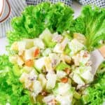 Waldorf salad and a serving spoon in a large bowl lined with leaf lettuce.