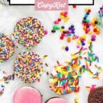 White chocolate covered oreos and sprinkles scattered on parchment paper.