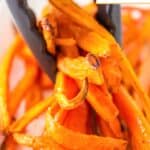 Tongs holding air fryer carrots.