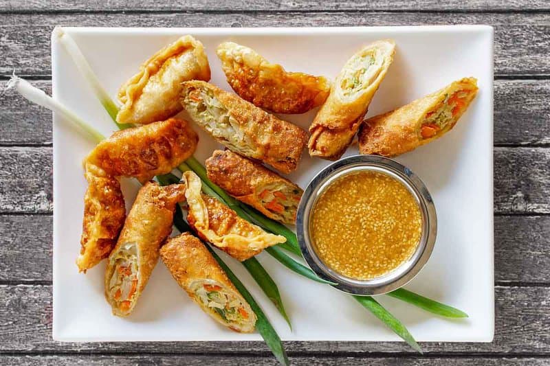 A small bowl of copycat Benihana magic mustard dipping sauce and egg rolls.