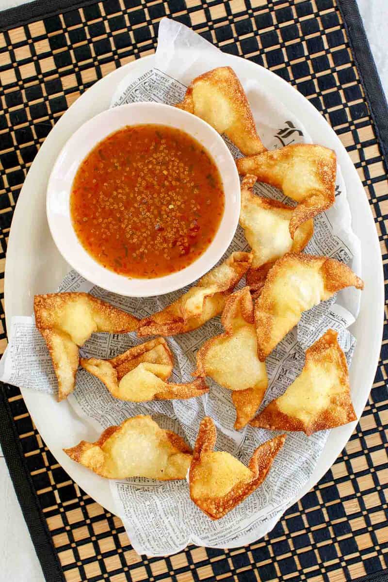 Cream cheese wontons and dipping sauce on a parchment paper covered platter.