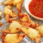 Several homemade cream cheese wontons and a small bowl of dipping sauce.