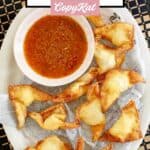 Homemade cream cheese wontons and a small cup of dipping sauce on a platter.