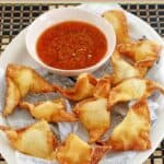 Homemade cream cheese wontons and dipping sauce on an oval platter.