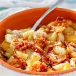 Crockpot cheesy potatoes and a spoon in a ceramic bowl.
