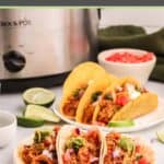 Chicken tacos on plates and a crockpot behind them.