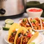 Chicken tacos on plates in front of a Crockpot.