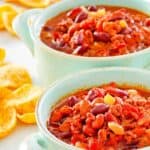 Two bowls of crockpot chili and Frito corn chips next to them.