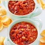 Two bowls of crockpot chili and Fritos scattered around them.