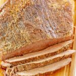 Oven baked beef brisket on a cutting board and a meat fork next to it.
