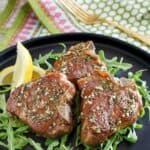 Pan seared lamb chops on a plate and a fork on a cloth napkin.