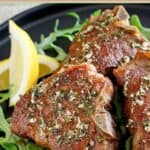 Pan seared lamb chops, lemon wedges, and arugula on a plate.