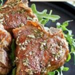 Cooked lamb chops and arugula on a plate.
