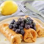 Homemade cheese blintzes topped with blueberries on a plate.