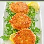 Three old-fashioned fried salmon patties over arugula on a platter.