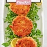 Old-fashioned salmon patties over arugula on a rectangular platter.