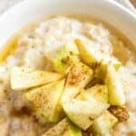 A bowl of oatmeal with cinnamon and apples on top.