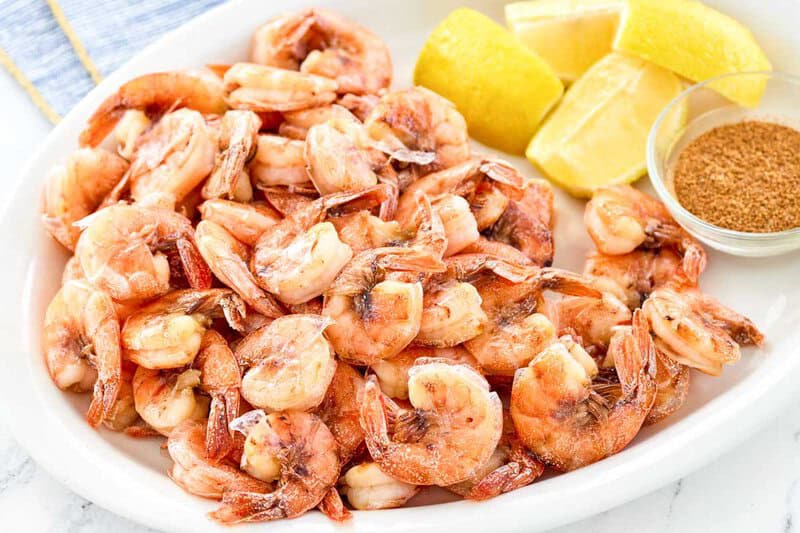 Boiled shrimp and four lemon wedges on a platter.