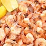 Boiled shrimp with shells and lemon wedges on a platter.