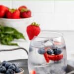 A glass of berry infused water, strawberries, and blueberries.