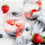 Two glasses of berry infused water and fresh berries in and around them.