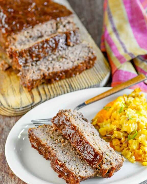 Copycat Cracker Barrel meatloaf slices on a plate in front of the meatloaf.