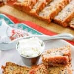 Homemade rhubarb bread slices and a small cup of cream cheese on a plate.
