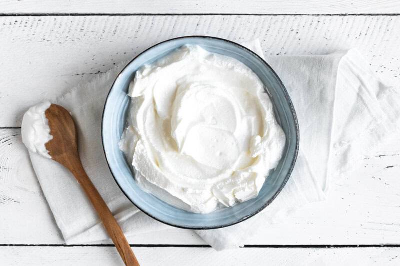 Sweetened yogurt in a small bowl and on a wooden spoon.