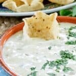A bowl of homemade white queso dip with a tortilla chip in it.