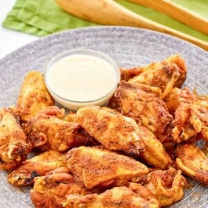 Copycat Wingstop Louisiana rub wings and a small cup of dipping sauce on a plate.