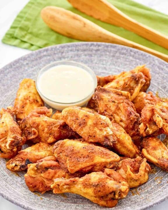 Copycat Wingstop Louisiana rub wings and a small cup of dipping sauce on a plate.