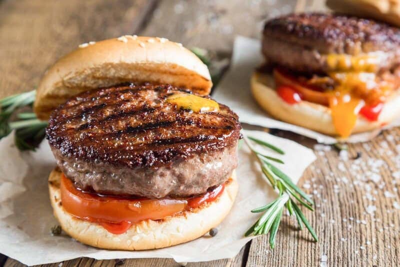 Grilled backyard burgers with ketchup, mustard, and tomato on sesame seed buns.
