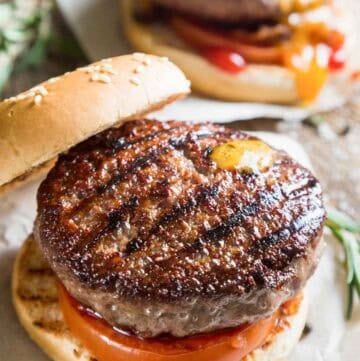 Grilled backyard burger with tomato on a sesame seed bun.