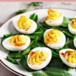 Classic deviled eggs and fresh spinach leaves on a plate.