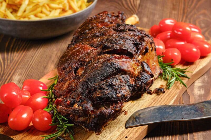 Oven roasted Indian style kashmiri leg of lamb and cherry tomatoes on a board.