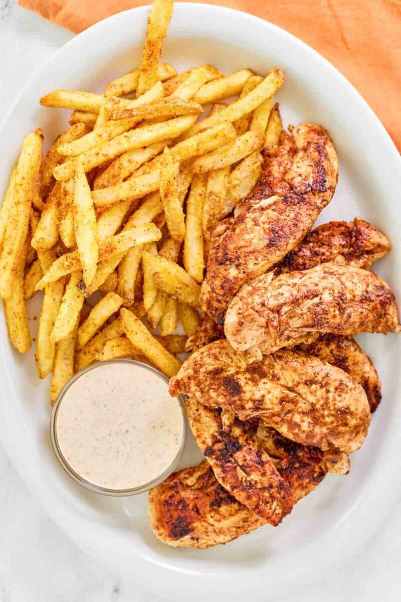 Copycat Popeyes blackened chicken tenders, cajun fries, and dipping sauce on a plate.