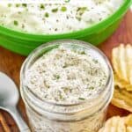 Homemade dry ranch dressing mix in a small glass jar next to a bowl of ranch dip.