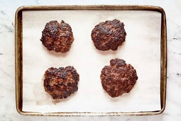 Four cooked burger patties on a tray.