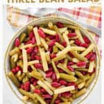 A bowl of grandma's three bean salad, serving spoon, and cloth napkin.