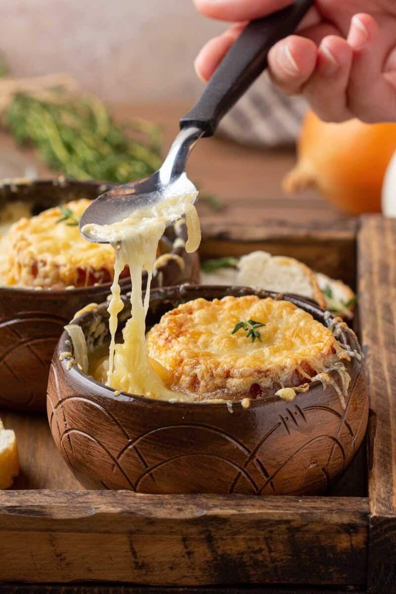 Homemade classic French onion soup in bowls and on a spoon.