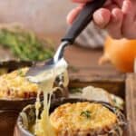 Homemade French onion soup and a spoon with cheese stretched from it and the soup.