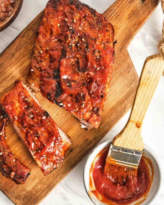 Homemade St. Louis style barbecue sauce in a small cup and on a rack of ribs.