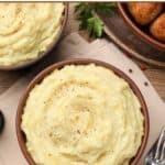 Two bowls of homemade mashed potatoes with pepper and two forks.