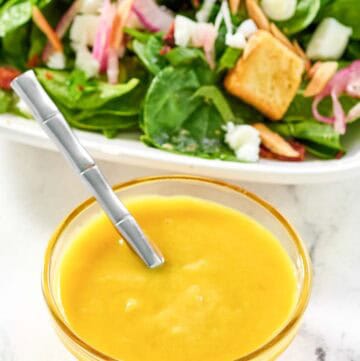 Copycat Simon and Seafort's mustard dressing in a small bowl and a salad behind it.