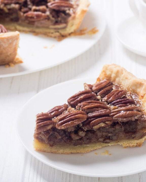 Copycat Taste of Texas pecan pie slice on a plate and the pie behind it.