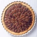 A whole copycat Taste of Texas pecan pie on a wood surface.