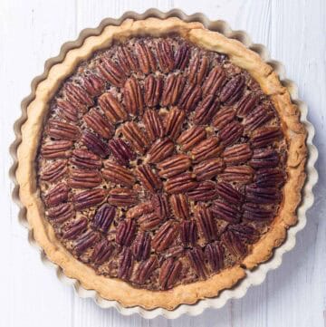 A whole copycat Taste of Texas pecan pie on a wood surface.