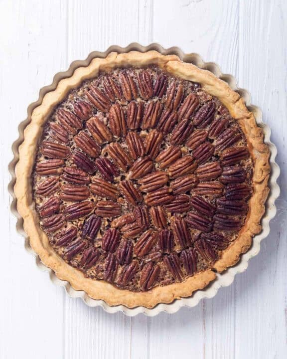 A whole copycat Taste of Texas pecan pie on a wood surface.