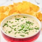 Homemade Applebee's queso blanco dip in a bowl and tortilla chips behind it.
