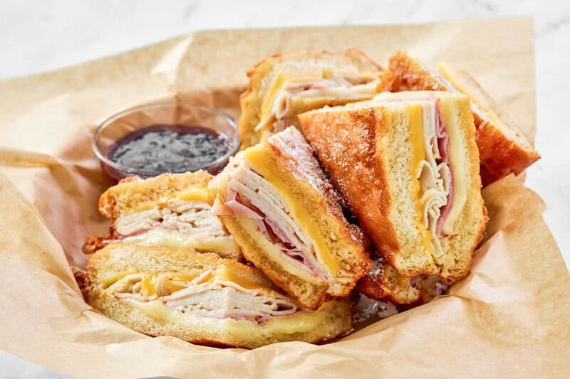 Copycat Cheddar's monte cristo sandwich and raspberry jam in a parchment lined basket.